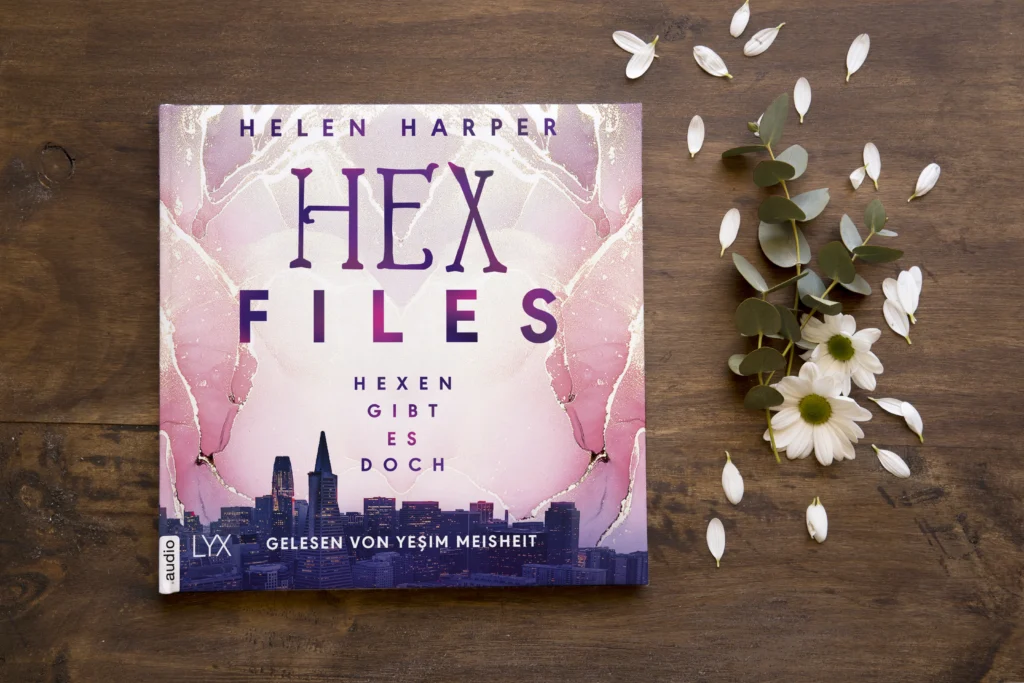 Hörbuch-Cover zu "Hexen gibt es doch" - Band 1 der Hex-Files Reihe von Helen Harper. Daneben ein paar weiße Blümchen auf hölzernem Untergrund.